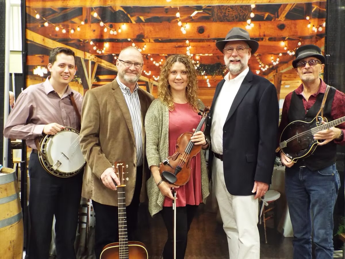 Whitewater Bluegrass Company band stands smiling with their instruments; banjo, guitar, fiddle, and mandolin